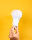 light bulb in hand on yellow background, electricity price increase concept Royalty Free Stock Photo