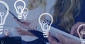 Light bulb icons floating against mid section of office colleagues using electronic devices Royalty Free Stock Photo