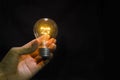 Light bulb in man hand on black background, old technology Royalty Free Stock Photo