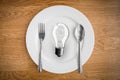 Light bulb in plate and fork and spoon on wooden table