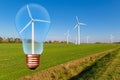 Light bulb with wind turbine inside on the background of blue sky and green field with turbines. Royalty Free Stock Photo