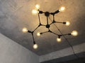 Light bulbs with warm lighting in stylish chandelier with exposed wiring on gray concrete ceiling, interior in retro loft design