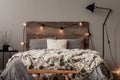 Light bulbs on wooden headboard of comfortable bed with grey bedding and warm fury blanket