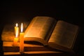 Light candle with holy bible and cross or crucifix on old wooden background in church.Candlelight and open book on vintage wood