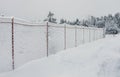 A light chain-link fence and a path in the village are covered with snow. Royalty Free Stock Photo