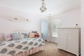 Light colored bedroom with a chandelier, a bed and a dresser in the corner next to the window