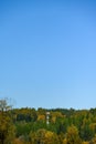 Light colored mobile phone tower with antennas on a hillside with evergreen trees and fall color deciduous trees, and clear blue s Royalty Free Stock Photo