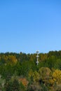 Light colored mobile phone tower with antennas on a hillside with evergreen trees and fall color deciduous trees, and clear blue s Royalty Free Stock Photo