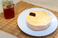 On a light countertop on a straw napkin on a white dish, a classic cheesecake and glassware a glass of tea with lemon and green