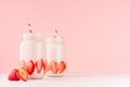 Light dairy strawberry drinks in trendy jars with ripe pieces berries, red striped straws on gentle pink background and white wood