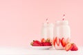 Light dairy strawberry drinks in trendy jars with ripe pieces berries on saucer, red striped straws on gentle pink background. Royalty Free Stock Photo