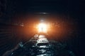 Light in end if tunnel and silhouette of man, dark wet underground brick corridor