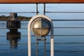 Light fixture on a ship railing, blue sky and still waters