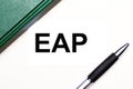 On a light gray background lies a pen, a green notebook and a white card with the text EAP Employee Assistance Program. Business Royalty Free Stock Photo