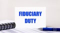 On a light gray background, a notebook, a blue pen and a sheet of paper with the text FIDUCIARY DUTY. Business concept