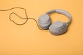 Light gray wireless on-ear headphones with the ability to connect via wire on a peach background. Headphones for playing