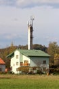 Light green new suburban family house with dark green roof tiles built in front of dirty old concrete industrial chimney Royalty Free Stock Photo