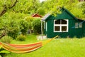 A light green small shed with white window frames, a gardenhouse in a beautiful wild garden with a colourful hammock in front of i Royalty Free Stock Photo