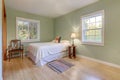 Light green walls bedroom interior with two windows and light hardwood floor with white bed and antique chair and casual rug Royalty Free Stock Photo