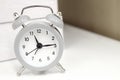 Light grey small alarm clock on white table. Countdown, deadline and time background.