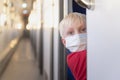 Light-haired boy in medical mask rides train compartment. Train travel rules during a pandemic and quarantine Royalty Free Stock Photo