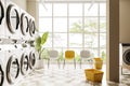 Light laundry interior with washing machines and chairs near panoramic window