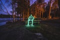 Light painting of human sitting on bench in night landscape with long exposure and glow of yellow fire light illuminated