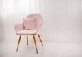 A light pink armchair stands by the window against a background of white airy curtains. A lonely chair in the room Royalty Free Stock Photo