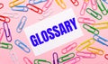 On a light pink background, colorful bright paper clips and a white card with the text GLOSSARY Royalty Free Stock Photo