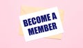 On a light pink background - a craft envelope. It has a white sheet of paper that says BECOME A MEMBER