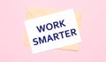 On a light pink background - a craft envelope. It has a white sheet of paper that says WORK SMARTER Royalty Free Stock Photo