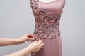 Light pink designer women`s dress handmade hanging on a white mannequin with an ornament of gold, gray and pink beads in the form