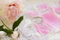 Light pink flower peony with bud rests on a white table groa with a glass dish with peony petals and a candle