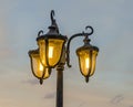 Light pole with three bulbs, orange light, blue sky, close up, outdoor.