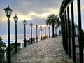 Light poles on the pathway lead to sea with cloundy sky.