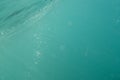 Light rays underwater beneath the surface of a turquoise breaking ocean wave, as bubbles rise to the surface, selective focus. Royalty Free Stock Photo