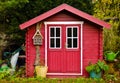 A light red small shed, gardenhouse, with some garden tools around it