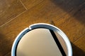 Light robot vacuum cleaner collects dust on a wooden laminate in the sun glare. Close up photo
