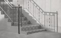 Light and shadow on surface of vintage stainless steel handrail with outside staircase in entranceway of home, black and white