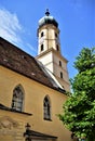 Light side of a church with bell tower, green fronds of a tree and blue cherry tree in Graz.