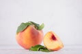 Light soft summer fruit background - ripe peach with bright fresh piece and green leaf on white wood table, copy space. Royalty Free Stock Photo