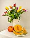 A light still life with a bouquet of colourful tulips and fruits, a melon and a pomegranate