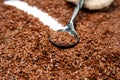 Dark grey metal spoon lies against a background of brown flax seeds. On a spoon are flax seeds