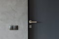 Light switch on the gray textured wall next to the door with metallic handle.