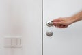 Light switch next to the door handle. Open white door with metallic handle. The man opens the door.