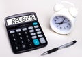 On the light table there is a black calculator with the text REVENUE on the scoreboard, a pen and a white alarm clock. Business Royalty Free Stock Photo