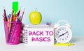 On a light table there are books, stationery, a white alarm clock, an apple. Next to it is a notebook with the text BACK TO BASICS Royalty Free Stock Photo