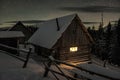 Light in window of wooden log cabin in winter mountains under stars Royalty Free Stock Photo