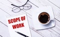 On a light wooden background, glasses, a pen, a cup of coffee and a notepad with the text SCOPE OF WORK Royalty Free Stock Photo