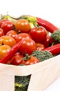 Light wooden basket filled with vegetables, cherry tomatoes, red hot chili peppers, broccoli and others Royalty Free Stock Photo